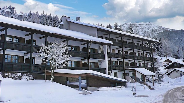 Un hotel de varios pisos con balcones, rodeado de árboles y montañas cubiertas de nieve.
