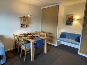 A dining area with a wooden table and chairs, a blue tablecloth, and a wall-mounted shelf with decorative items.
