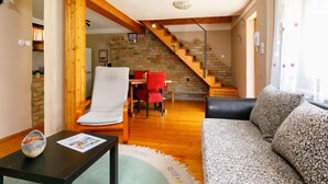 Una sala de estar acogedora con una escalera de madera, un sofá, una mesa de comedor con sillas y una mesita con una revista.