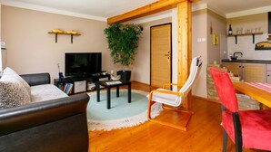 Una sala de estar con sofá, televisor, mesa de comedor con sillas, planta y área de cocina con lavaplatos y armarios.