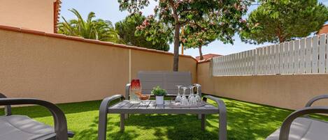 A patio with a table set for dining, surrounded by chairs, and a white fence in the background.