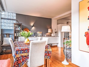 A modern dining area with a patterned tablecloth, a vase of flowers, and a bookshelf.