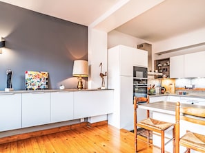 A modern kitchen with white cabinetry, a wooden floor, and a dining area with a table and chairs.