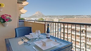 Ein Balkon mit Tisch für zwei Personen, mit Blick auf eine Stadtlandschaft und einen Berg.