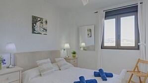 Ein Schlafzimmer mit einem Bett, zwei Nachttischen, einem Spiegel, einem Fenster mit Vorhängen und einem Sessel.