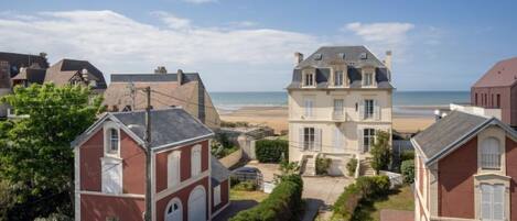 A coastal residential area with a prominent two-story house featuring a balcony and a smaller adjacent building.