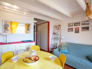 A dining area with a yellow table, chairs, and a bowl of fruit. There is a blue sofa and a bookshelf in the background.