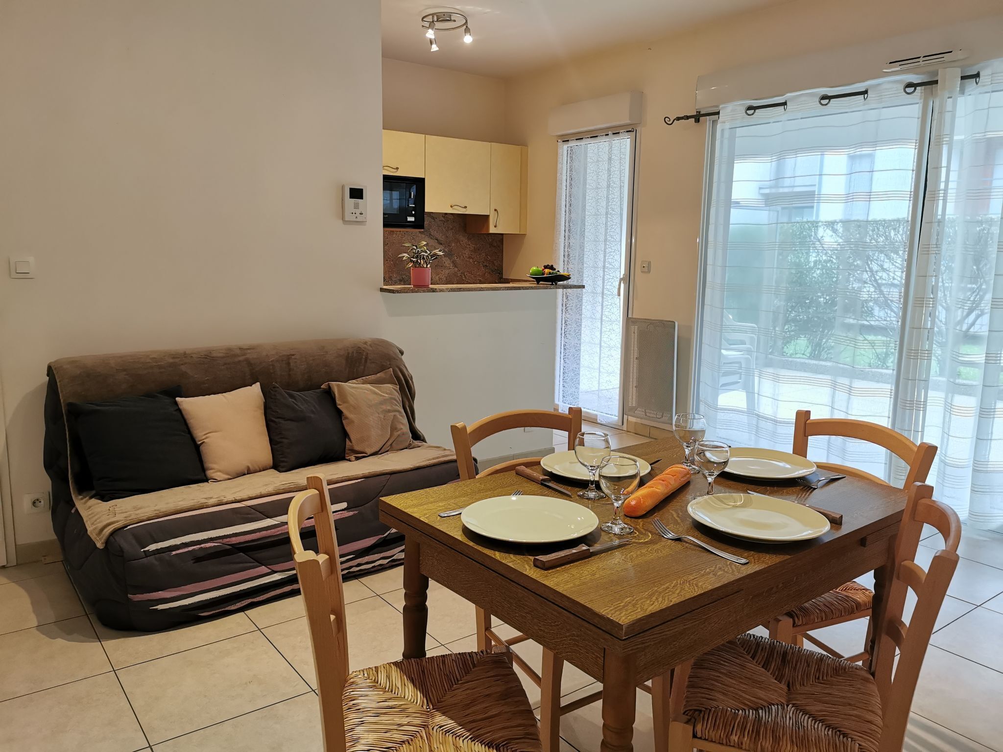 Een eetgedeelte met een houten tafel gedekt voor twee personen, een bank en een keuken op de achtergrond.