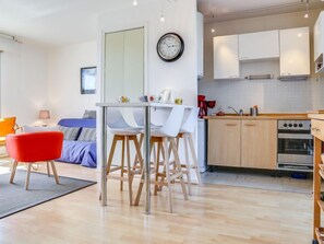 Een modern appartement met een eethoek, keuken en woonkamer met een bank en een rode fauteuil.