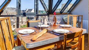 Mesa de jantar posta para quatro com vista para edifícios através de grandes janelas.
