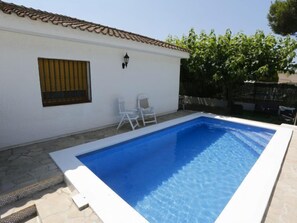 A rectangular swimming pool with a white border, two white chairs, and a window with bars. - Vacation home Juan by Interhome (Deltebre)