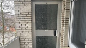 A door with a frosted glass panel and a metal handle, set in a brick wall with a window to the right. - Deichblick by Interhome (Norddeich)