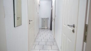 A narrow hallway with white tiled flooring and white doors on both sides. - Deichblick by Interhome (Norddeich)