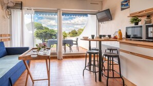 A cozy room with a sofa, a dining table, and a kitchen area with a TV, microwave, and bar stools.