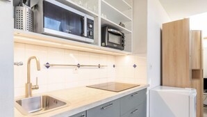 Eine moderne Küche mit einer Edelstahl-Spüle, grauen Schränken, einer eingebauten Mikrowelle und einem weißen Kühlschrank.