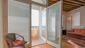 A modern living room with a glass door leading to a balcony, a wicker chair, a small table, and a sofa with a striped cushion. - Apartment Iris by Interhome (Venezia Giudecca)