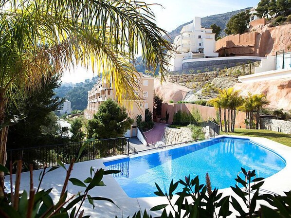 A swimming pool with a curved edge, surrounded by greenery and a mountainous backdrop.