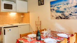 Zona pranzo con tavolo apparecchiato per quattro persone, una bottiglia di vino e un quadro che raffigura un paesaggio innevato.