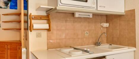A compact kitchen with a microwave, sink, and wooden cabinets.