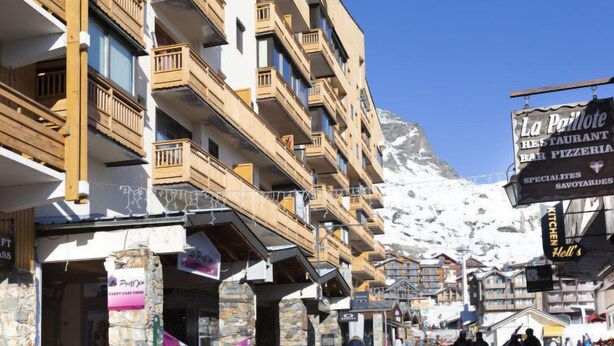 A multi-story hotel with balconies, a restaurant sign, and a mountain backdrop. - Vanoise 152 by Interhome (Val Thorens)