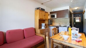 A compact kitchenette with a microwave, stove, and sink. There's a wooden table with chairs and a red sofa. - Vanoise 152 by Interhome (Val Thorens)