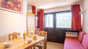 A cozy room with a wooden dining table, chairs, a pink sofa, and a window with curtains. - Vanoise 152 by Interhome (Val Thorens)