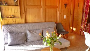 A wooden interior with a grey sofa, a small round wooden table with a vase of flowers, and a black chair. - Centaure A RS 3 by Interhome (Ovronnaz)