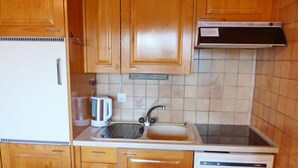 A compact kitchen with wooden cabinets, a white refrigerator, a coffee maker, a sink, and a dishwasher. - Centaure A RS 3 by Interhome (Ovronnaz)