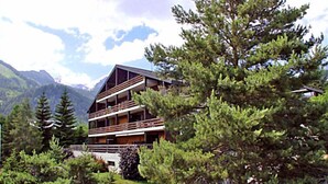 A multi-story building with balconies, surrounded by trees and mountains. - Centaure A RS 3 by Interhome (Ovronnaz)