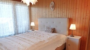 A bedroom with a large bed, two bedside tables with lamps, a wooden headboard, and a patterned rug. - Centaure A RS 3 by Interhome (Ovronnaz)