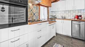Ett modernt kök med vita skåp, en diskmaskin i rostfritt stål, en röd kaffebryggare och ett mönstrat stänkskydd.