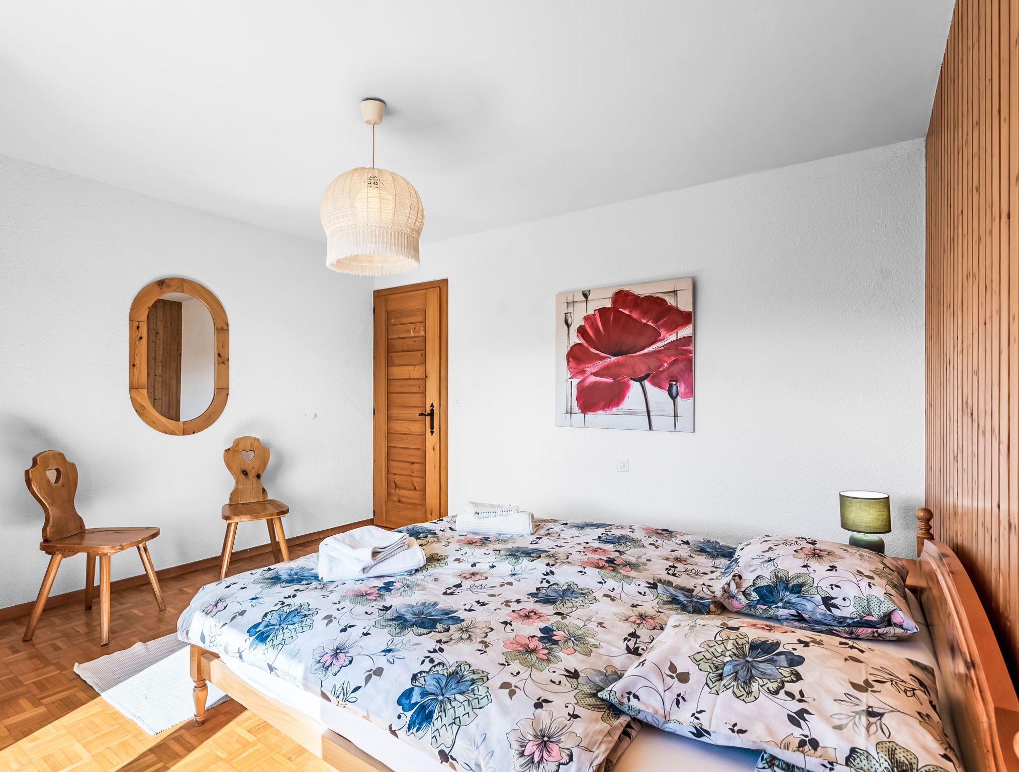 Un dormitorio con una cama de madera, un espejo, una puerta y un cuadro floral en la pared.