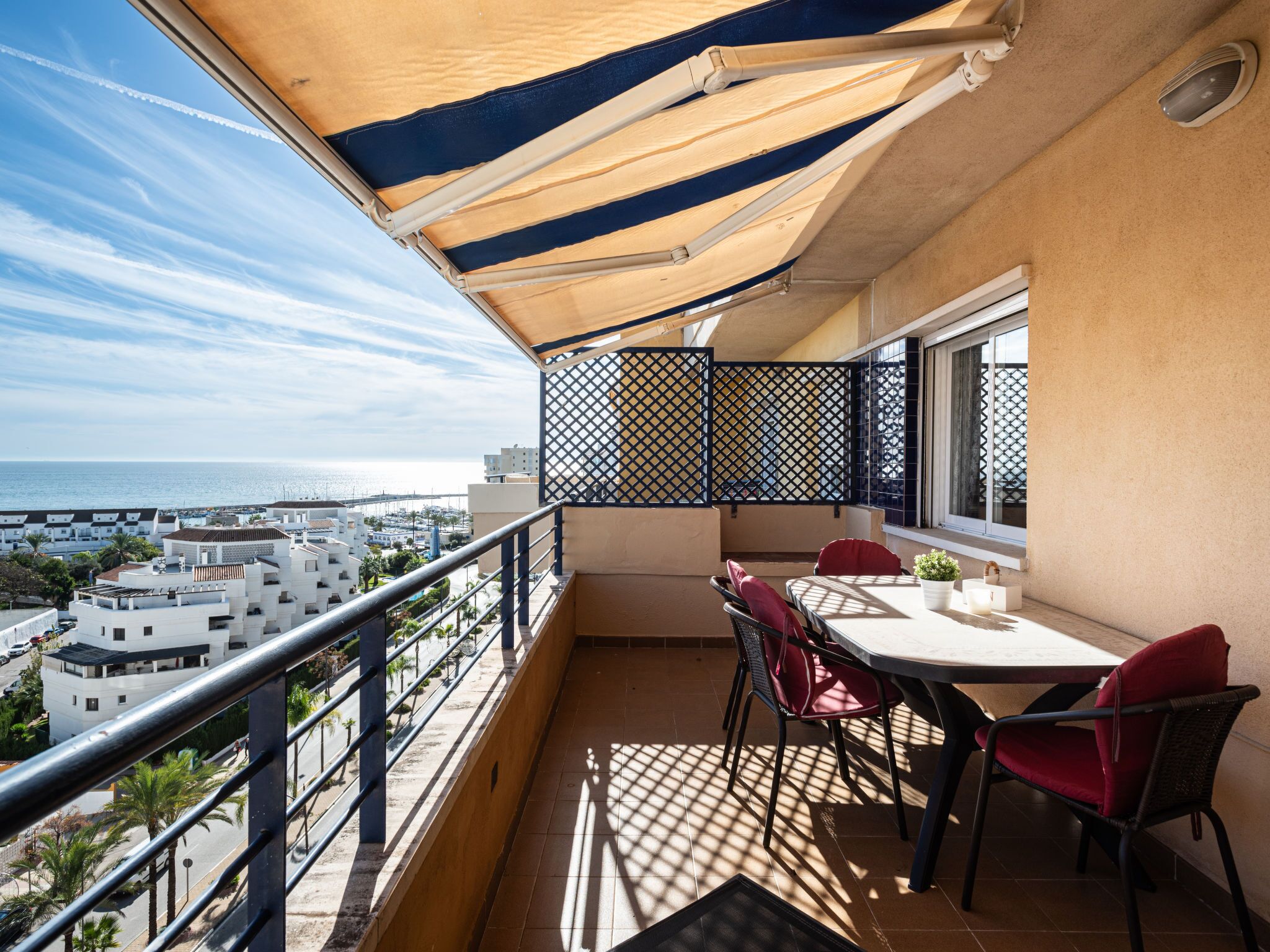 A balcony with a table and chairs, a view of the sea, and a cityscape in the background.
