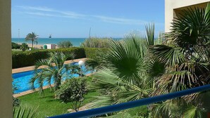Zona de piscina con vista al mar, rodeada de vegetación y palmeras.