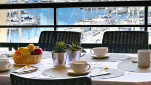 A dining area with a view of a marina, featuring wicker chairs, a table set with cups, a fruit basket, and a small plant. - Bleu Marine by Interhome (Fréjus)