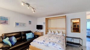 A bedroom with a bed, a black leather sofa, a TV, and a wooden headboard. - Apartment Luchre by Interhome (Zermatt)
