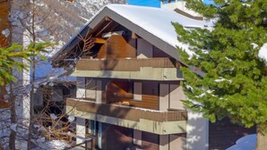 A multi-story chalet with a sloped roof, wooden balconies, and a snow-covered landscape. - Apartment Luchre by Interhome (Zermatt)