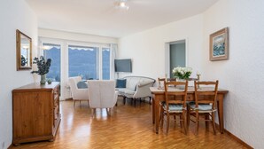 Une pièce spacieuse avec un plancher en bois, une table à manger avec des chaises, un canapé, un téléviseur et une vue sur les montagnes grâce à de grandes fenêtres.