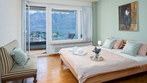 Une chambre avec un lit, une chaise, un tableau et une vue sur un lac et des montagnes.