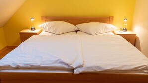 A neatly made bed with white linens and pillows, flanked by two bedside lamps on wooden nightstands. - Am Nordkap by Interhome (Norddeich)