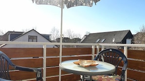 A balcony with a table and two chairs, an umbrella, and a view of houses in the background. - Am Nordkap by Interhome (Norddeich)