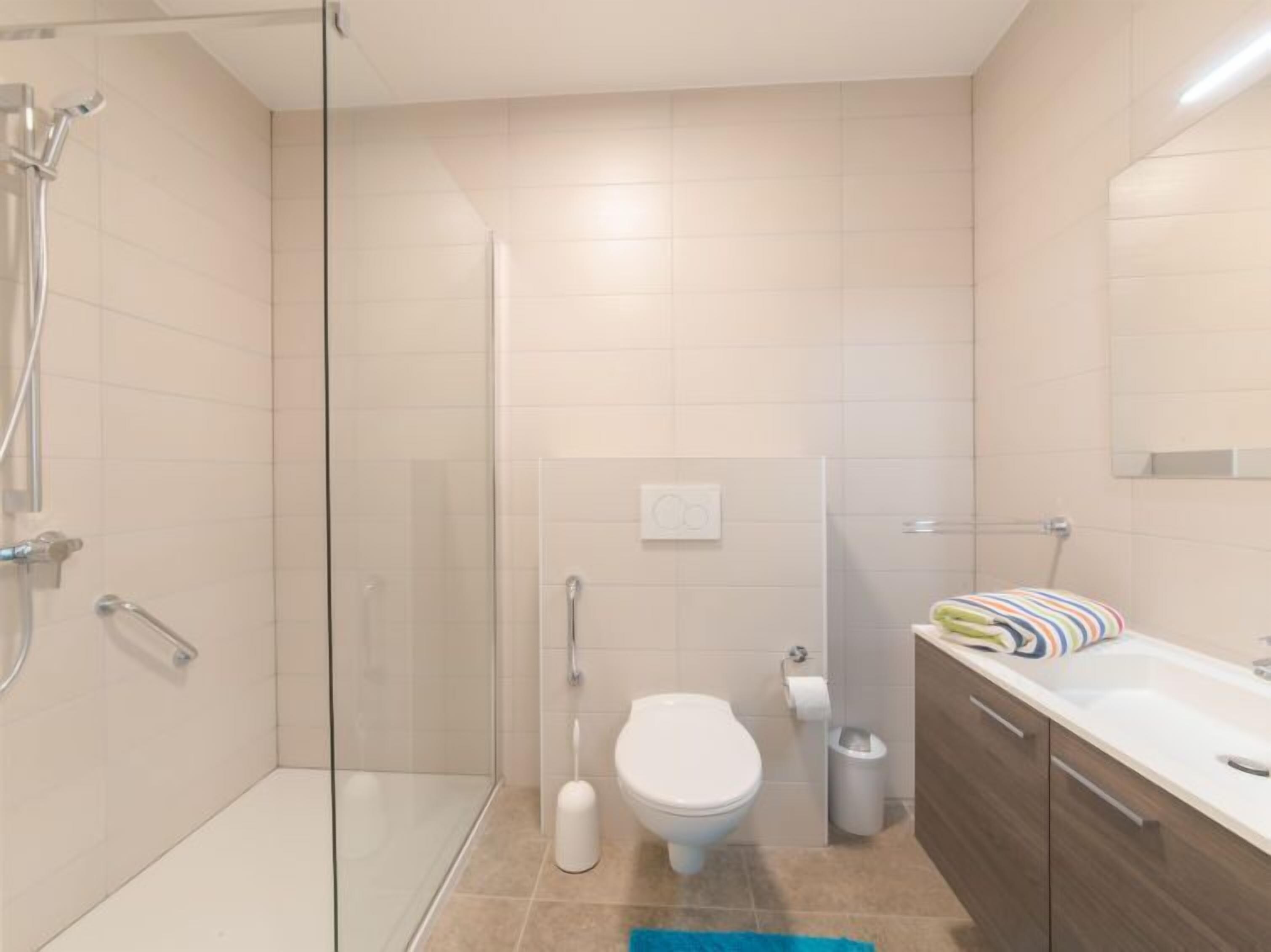 A modern bathroom with a glass-enclosed shower, a toilet, a sink, and a towel rack.