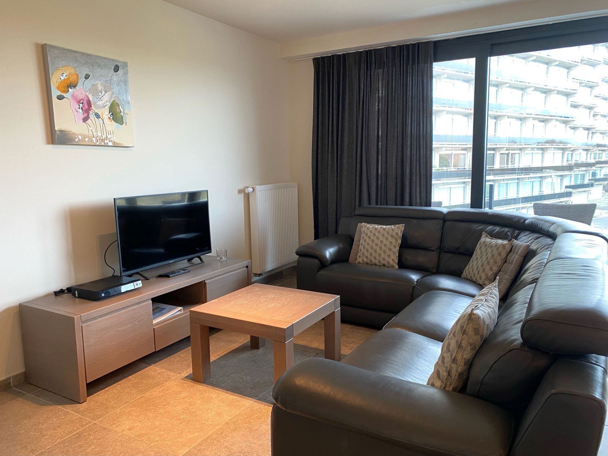 Ein modernes Wohnzimmer mit Flachbildfernseher, einer Couch, einem Couchtisch und einem Gemälde an der Wand.