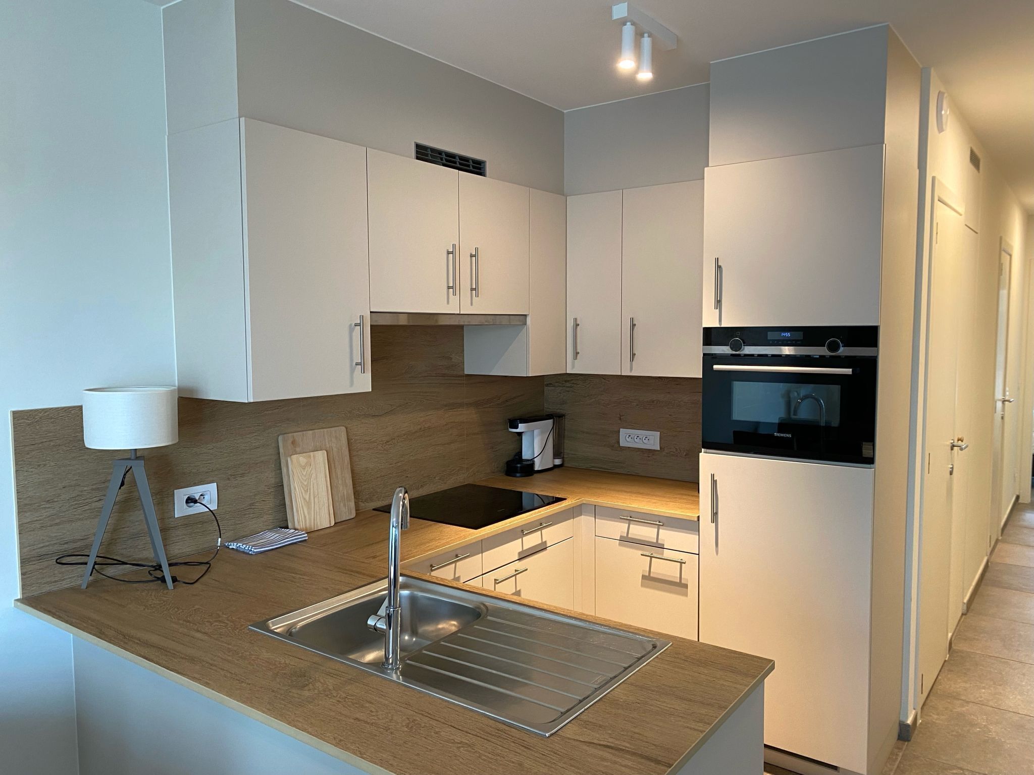A modern kitchen with white cabinets, a stainless steel sink, and a built-in oven.