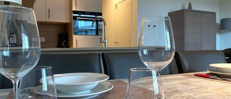 Une table à manger dressée avec des verres à vin et des assiettes, une cuisine en arrière-plan et un buffet.