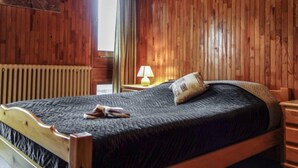 Ett rum med träpanel på väggarna, en säng, ett nattduksbord, en lampa och ett fönster med gardiner.