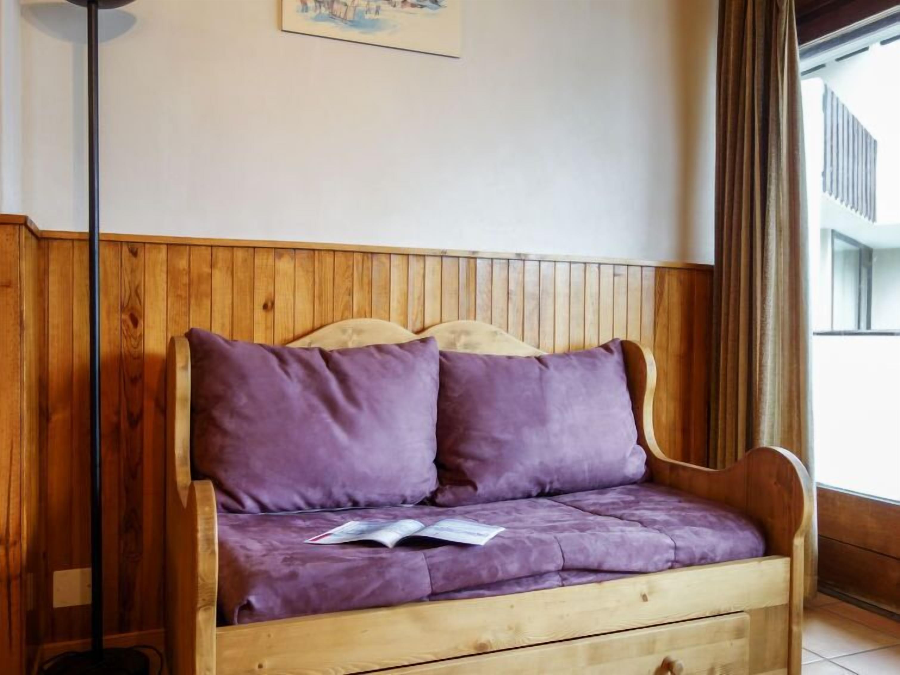 Een houten bank met twee paarse kussens en een boek erop.