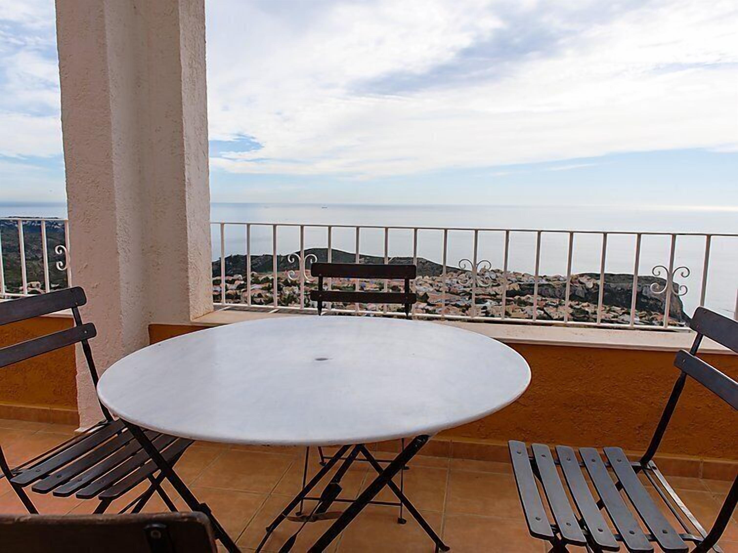 Une table ronde avec deux bancs sur un balcon donnant sur une ville côtière.
