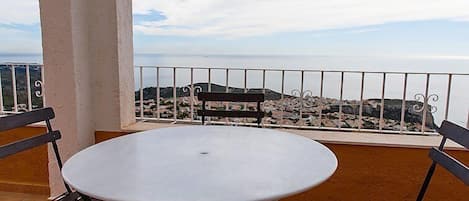 Une table ronde avec deux bancs sur un balcon donnant sur une ville côtière.