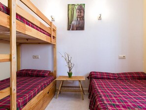 A dormitory room with bunk beds, a small table with a vase, and a Buddha statue on the wall.